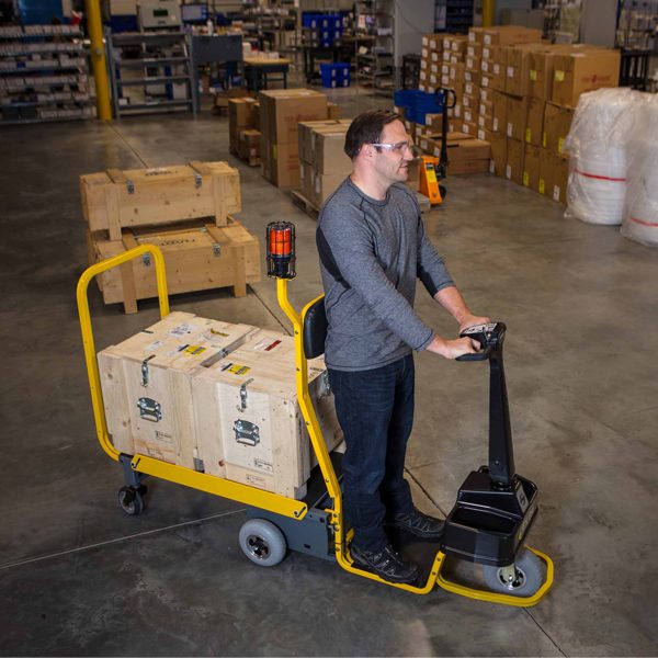 Worker operating a standing industrial cart with boxes on it in a warehouse.