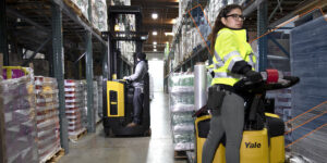 Two workers each on a forklift in a warehouse